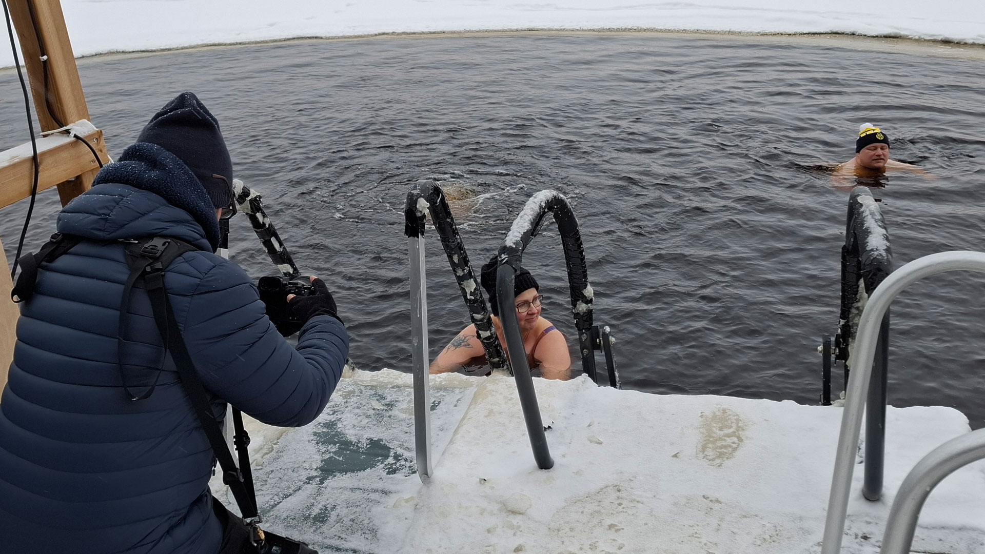 Etualalla valokuvaaja selin kuvaa avannossa olevaa uimaria.