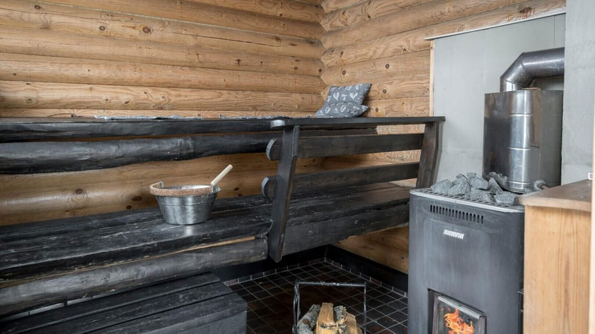 Saunan lauteet. Puulämmitteisessä kiukaassa palaa tuli.
