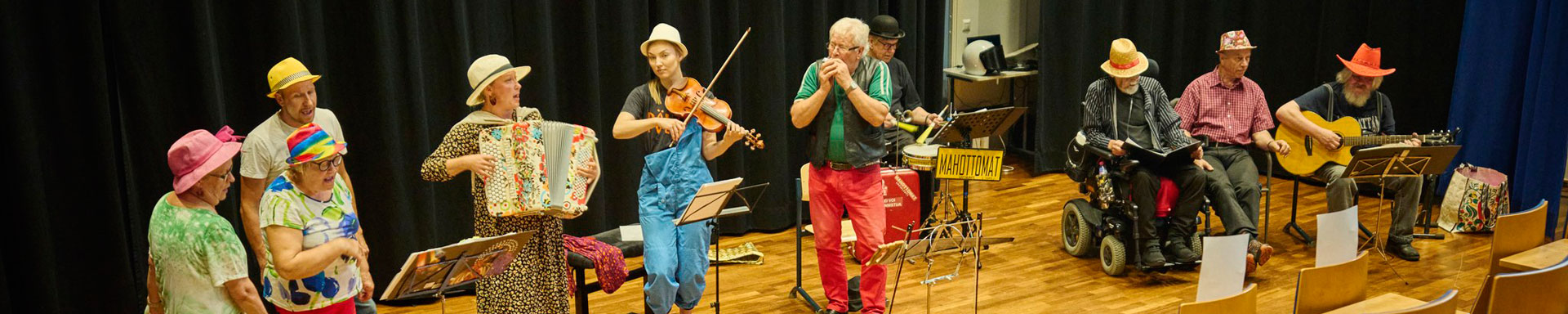 10 henkilöä laulamassa ja soittamassa eri soittimia esiintymislavalla.