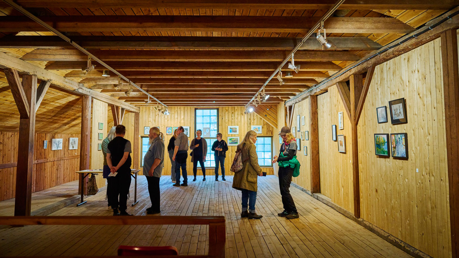 Yhdeksän ihmistä näyttelytilassa, jonka seinällä on tauluja.