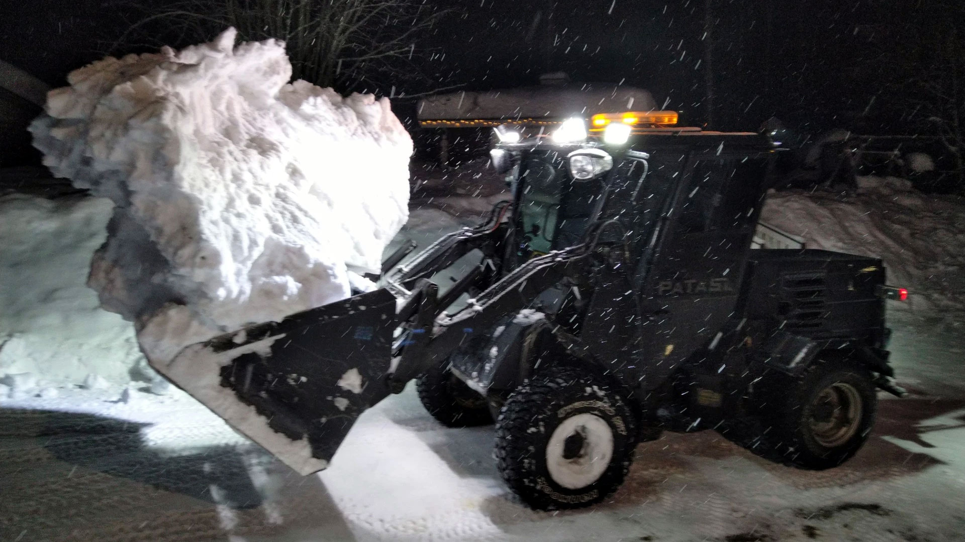 Traktori, jonka etukauhassa on iso lumilohkare.