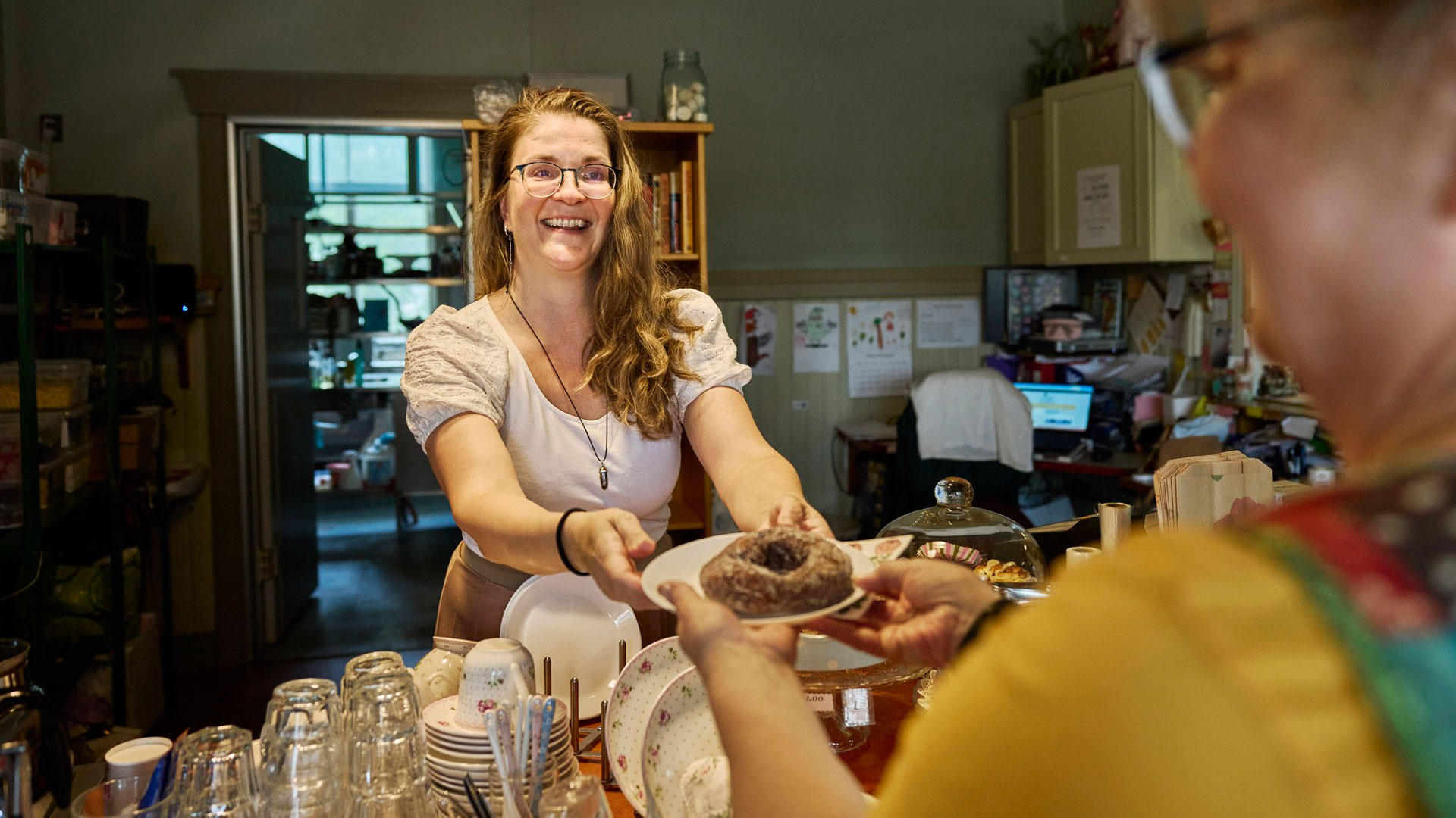 Kahvilan myyjä ojentaa lautasella olevan munkkirinkilän asiakkaalle.